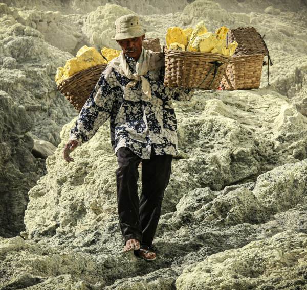 mario-la-pergola-84WidVjX2as-unsplash (1) Mann trägt Körbe mit Steinen über Felsen